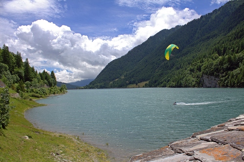 Immagine con lago, alberi, nuvole, acqua, cielo, montagna, verde, parapendio, vela, azzurro, montagne, sport, rocce, scia, bosco