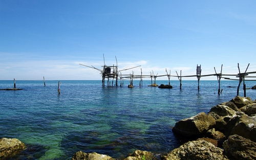 Immagine con mare, acqua, cielo, scogli, azzurro, pali, pontile, orizzonte, trabucco, nuvole, rocce, paletti, pescare, legno, pesca, scogliera