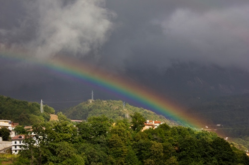 Immagine con nuvole, arcobaleno, alberi, cielo, case, temporale, montagne, paesaggio, colori