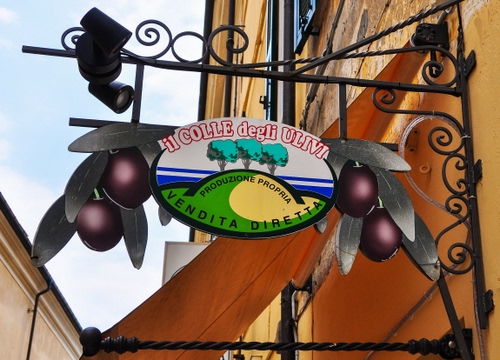 Immagine con olive, insegna, ferro, scritta, negozio, foglie, verde, alberi