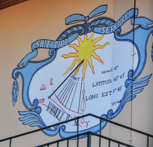 Immagine con sole, meridiana, azzurro, giallo, ringhiera, numeri, orologio, muro, scritte, scritta, asta