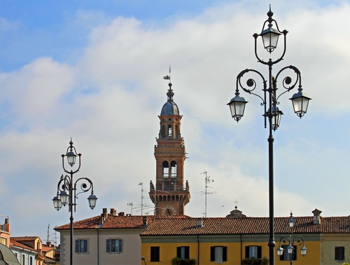 Immagine con lampioni, finestre, nuvole, cielo, campanile, case, antenne, tetti, torre, comignoli, lampione, comignolo, orologio, azzurro