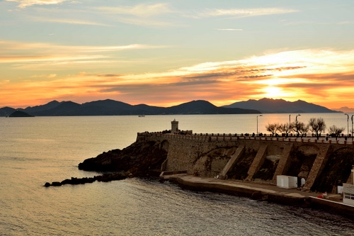 Immagine con mare, tramonto, molo, acqua, montagne, torre, panorama, porto, sole