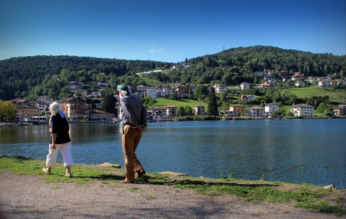 Immagine con lago, due, acqua, persone, panorama, colline, case, donna, uomo, montagne, passeggiata, paese, passanti