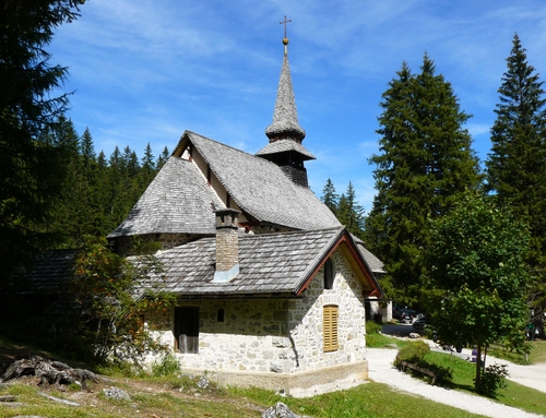 Immagine con chiesa, alberi, campanile, verde, tetti, cielo, montagna, croce, tetto, finestre, bosco