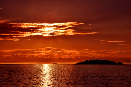 Immagine con mare, isola, tramonto, nuvole, rosso, sole, controluce, riflesso