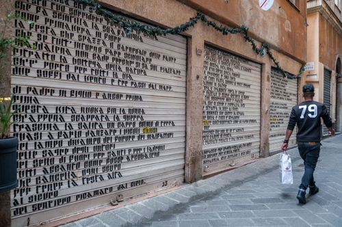 Immagine con scritte, serrande, passante, strada, numero, saracinesche, uomo, numeri