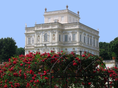 Immagine con fiori, palazzo, statue, rose, rosso, verde, bianco, cielo, finestre, piante, villa, alberi, azzurro, arco, siepe, ferro, archi