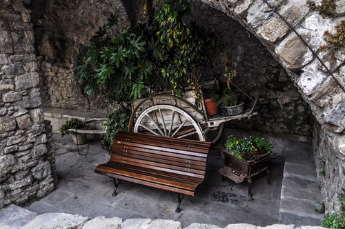 Immagine con panchina, arco, piante, ruota, carretto, legno, verde, vasi, pietre, carro, pietra, foglie