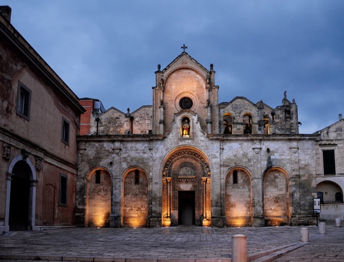 Immagine con chiesa, piazza, sera, luci, archi, portale, facciata, cielo