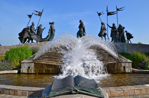 Immagine con fontana, acqua, libro, statue, bandiere, zampilli, monumento, cielo, stendardi, verde, spruzzi, azzurro, piante