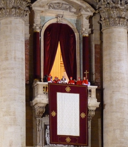 Immagine con colonne, papa, croce, balcone, rosso, bianco, cardinali, prelati, tende, tappeto, arco, tenda, vaticano, capitelli, roma, drappo, tendaggi