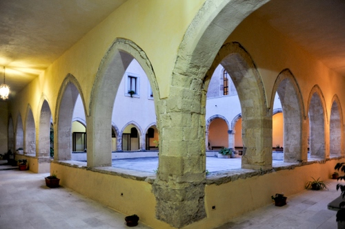 Immagine con archi, chiostro, finestre, colonne, portico, vasi, piante, pilastri, luce, porte, cortile, luci, porticato, lampione