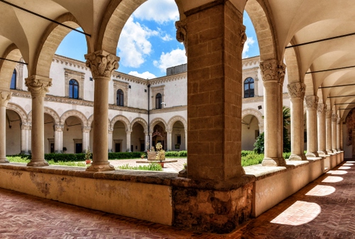 Immagine con archi, colonne, chiostro, nuvole, pozzo, cielo, ombre, finestre, giardino, capitelli, verde, portico, piante, pilastro, ombra