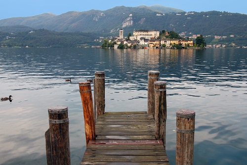 Immagine con isola, lago, montagne, pontile, acqua, legno, anatre, pali, campanile, borgo, case, cielo, papera, montagna, chiesa, molo