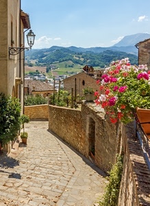 fiori, lampione, montagne, strada, cielo, vasi, via, case, piante, azzurro, paese, borgo, alberi, tetti, gerani, muro, discesa, colline, nuvole, vicolo, selciato